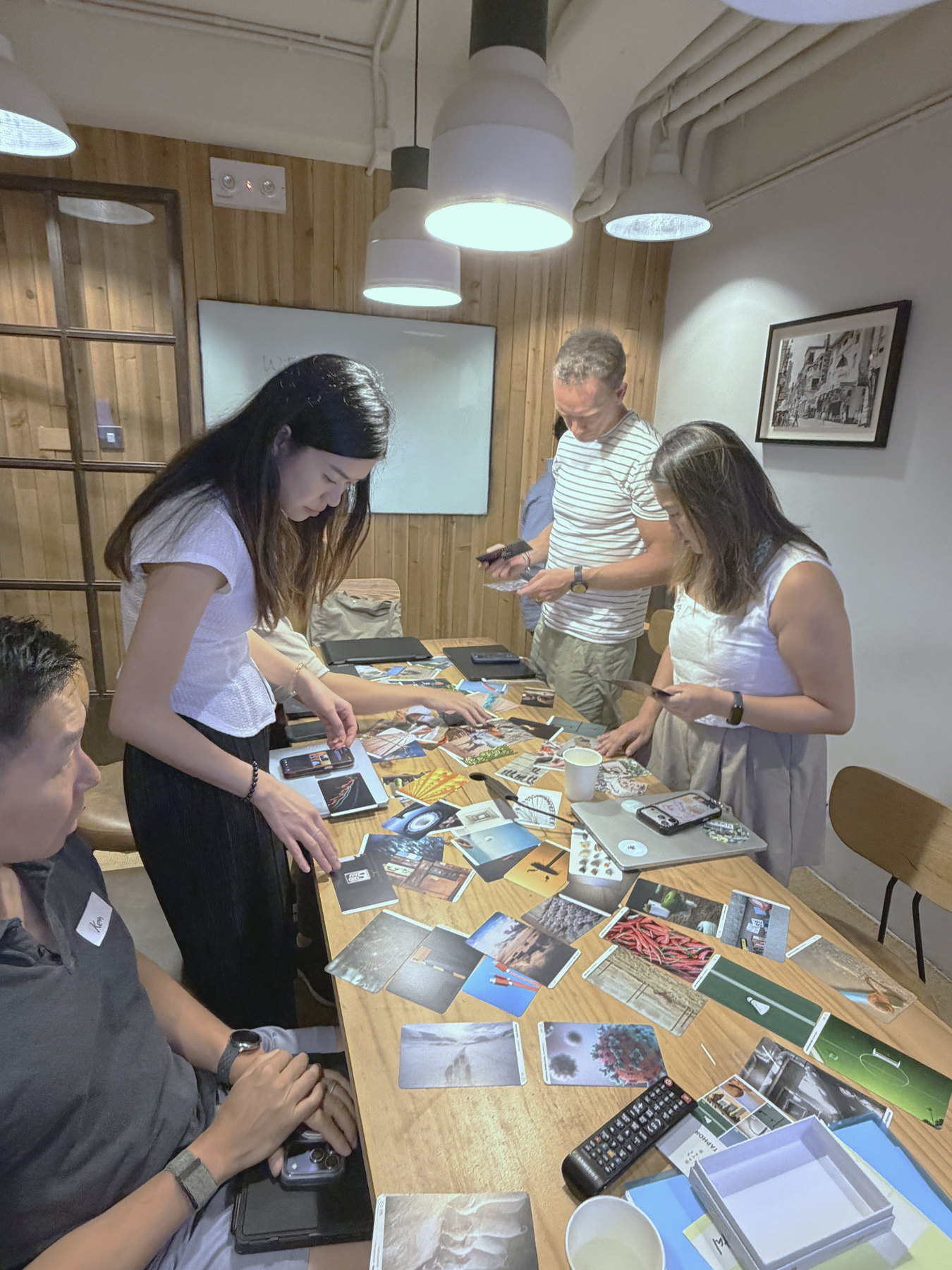 Participants standing around a long table covered with printed image cards, notebooks and laptops.